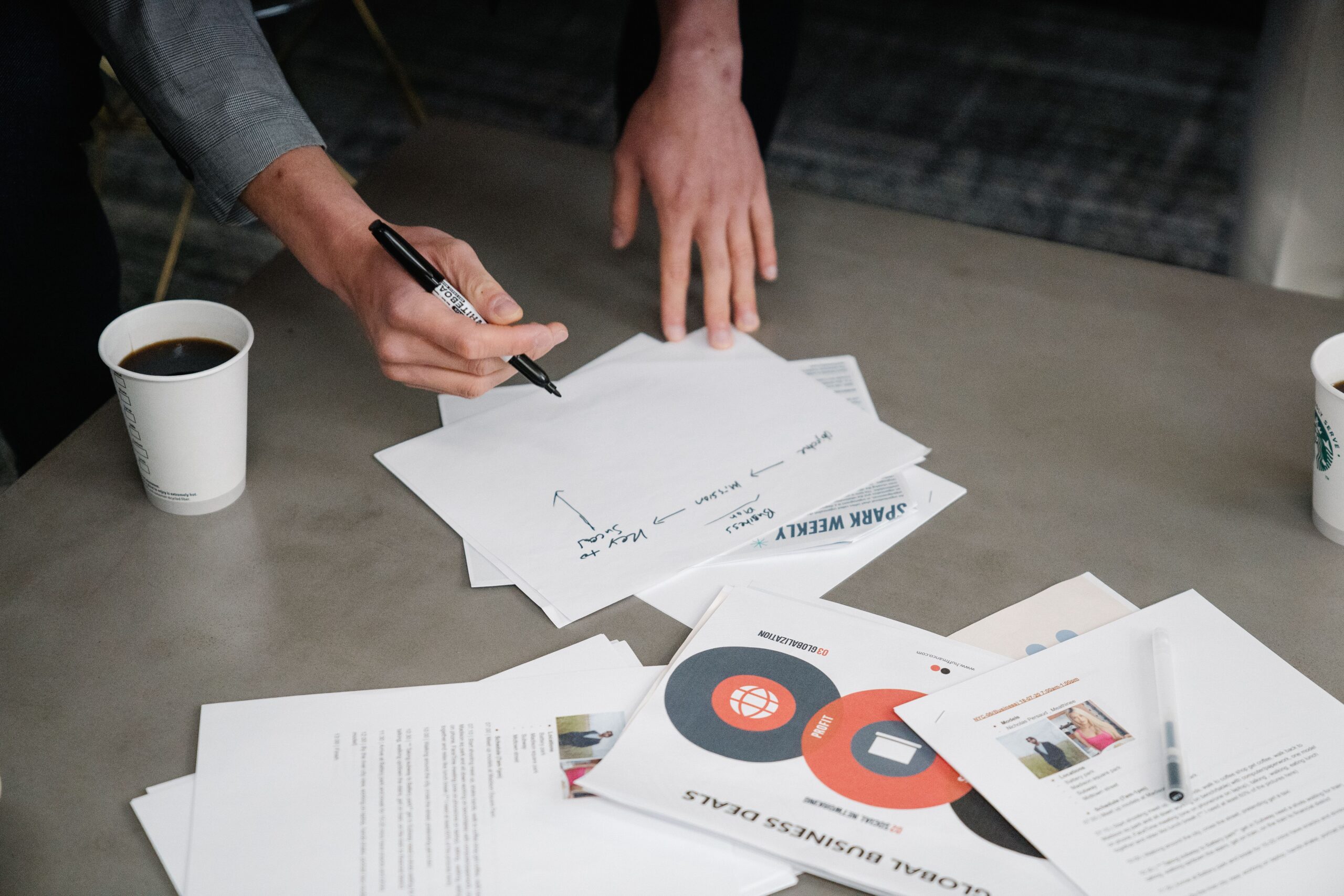 Two people collaborate during a business meeting, writing notes on papers with coffee cups nearby.